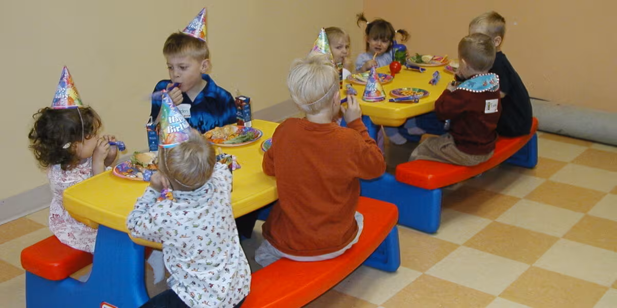 Niños con gorros de fiesta sentados alrededor de una mesa infantil