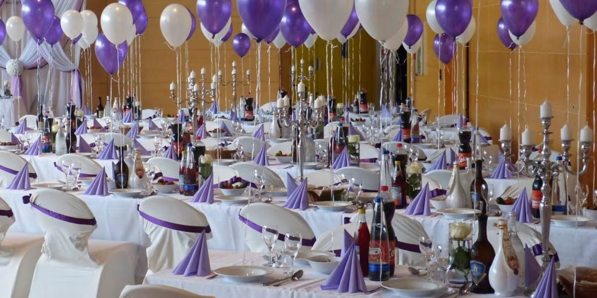 Salón de fiestas montado con mesas, mantelería blanca y globos morados