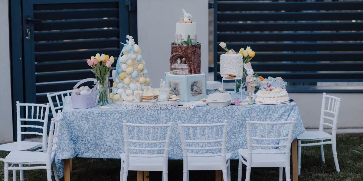 Mesa de postres montada al aire libre con mantel y sillas blancas