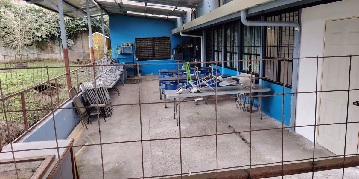 Sillas plegables apiladas junto a mesas en un área techada