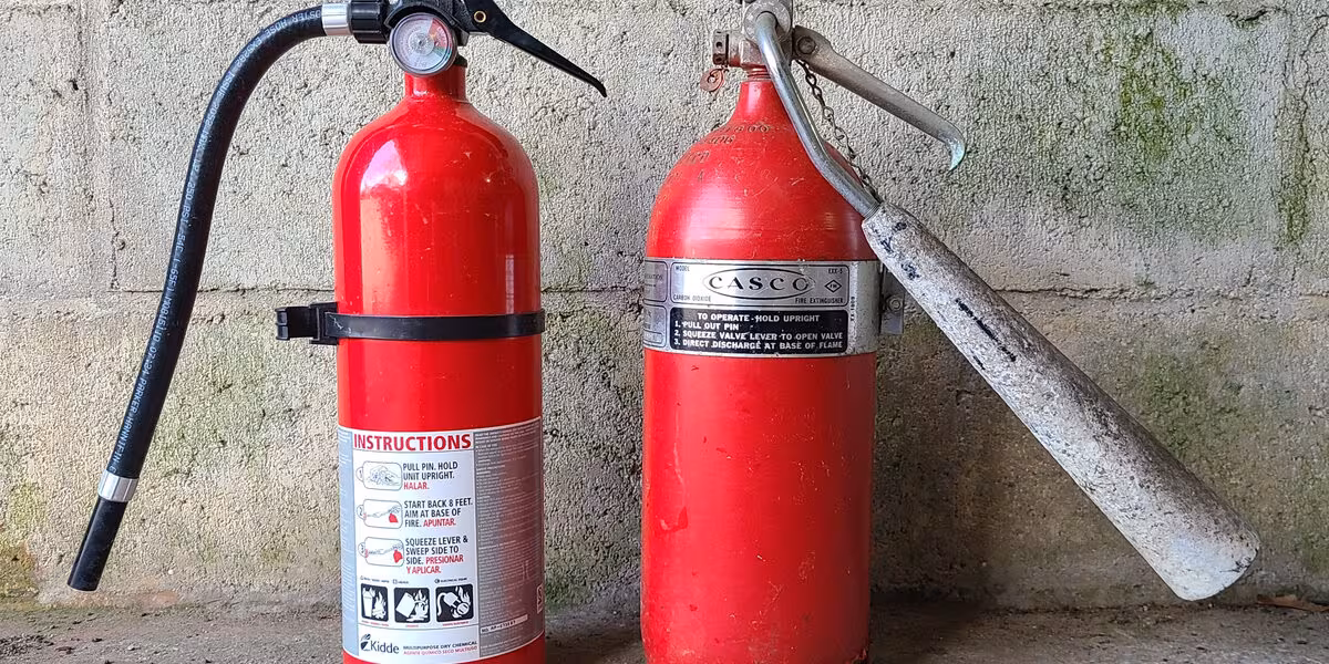 Dos extintores rojos con etiquetas de instrucciones apoyados en un muro