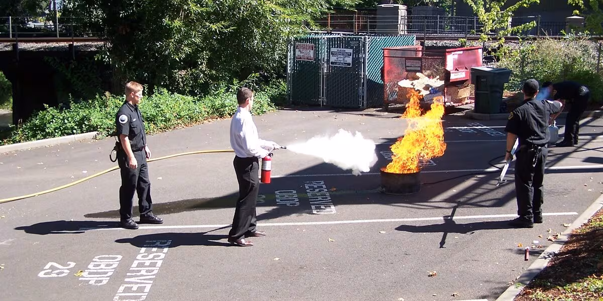 Personas practicando con un extintor sobre un fuego controlado durante una capacitación al aire libre