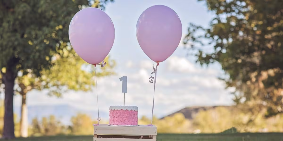 Globos lilas junto a un pastel pequeño con el número uno