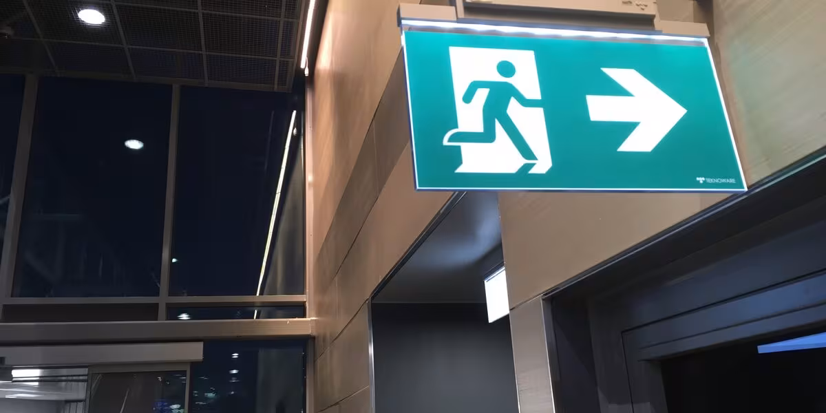 Señal verde de salida de emergencia con flecha direccional sobre una puerta